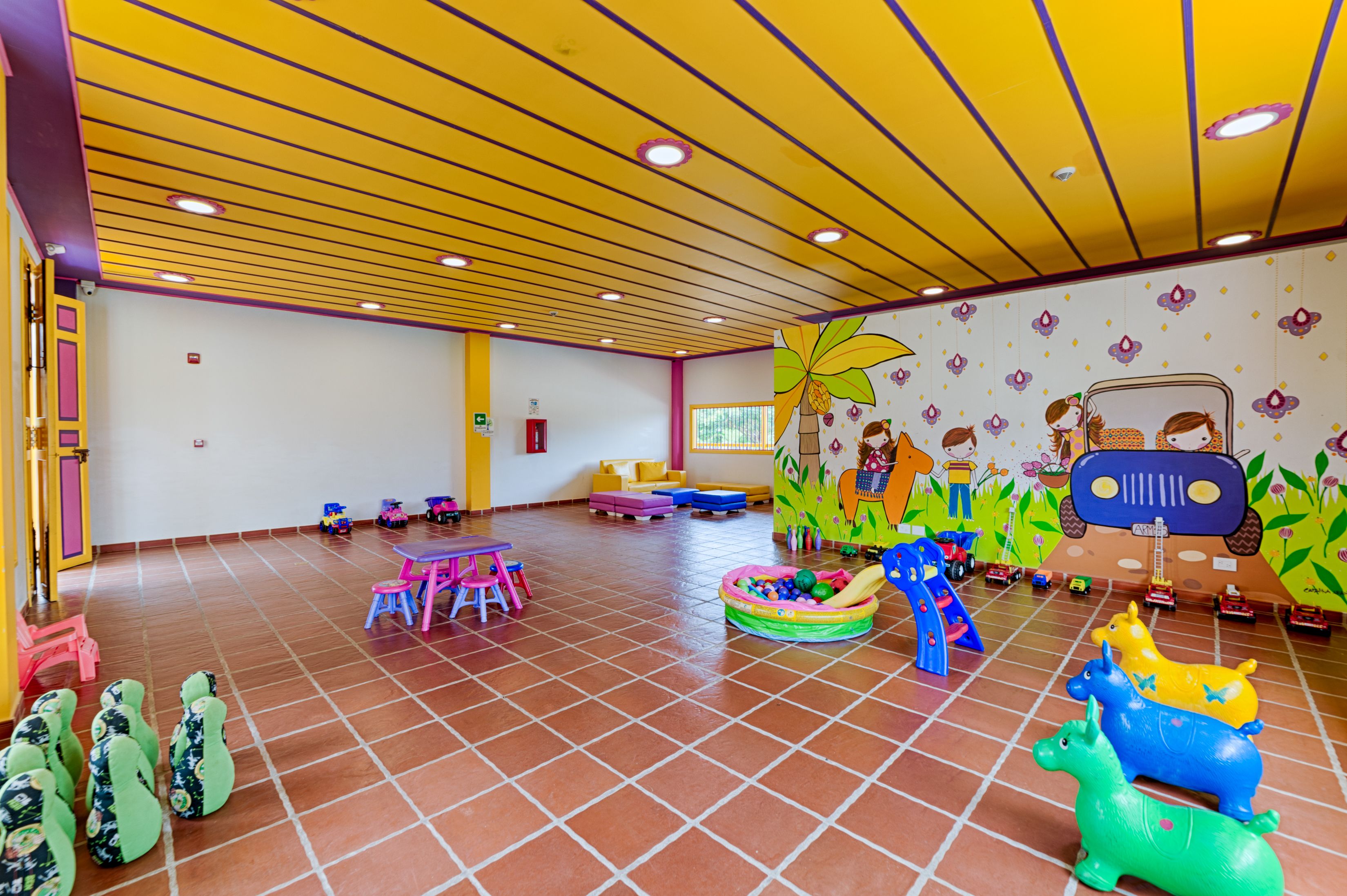 Un área de juegos infantiles con juguetes coloridos, un tobogán y un mural en la pared.