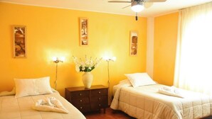 A hotel room with two beds, a nightstand, a vase with flowers, and wall art. - Hospedaje Claudia (Ica)