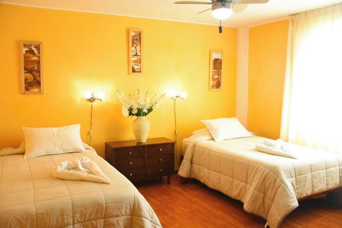 Una habitación de hotel con dos camas, una mesita de noche, un jarrón con flores y decoración en la pared.