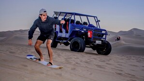A person on a snowboard in a desert with a blue vehicle in the background. - Hospedaje Claudia (Ica)