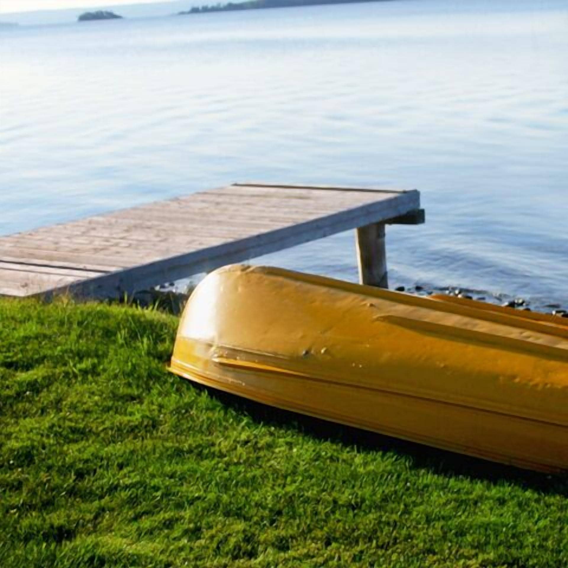A yellow boat on a grassy area near a wooden dock extending into calm water.