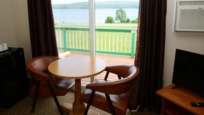 A room with a view of a lake, a round wooden table with two chairs, a television, and a heater on the wall. - Cabot Trail Motel (Baddeck)