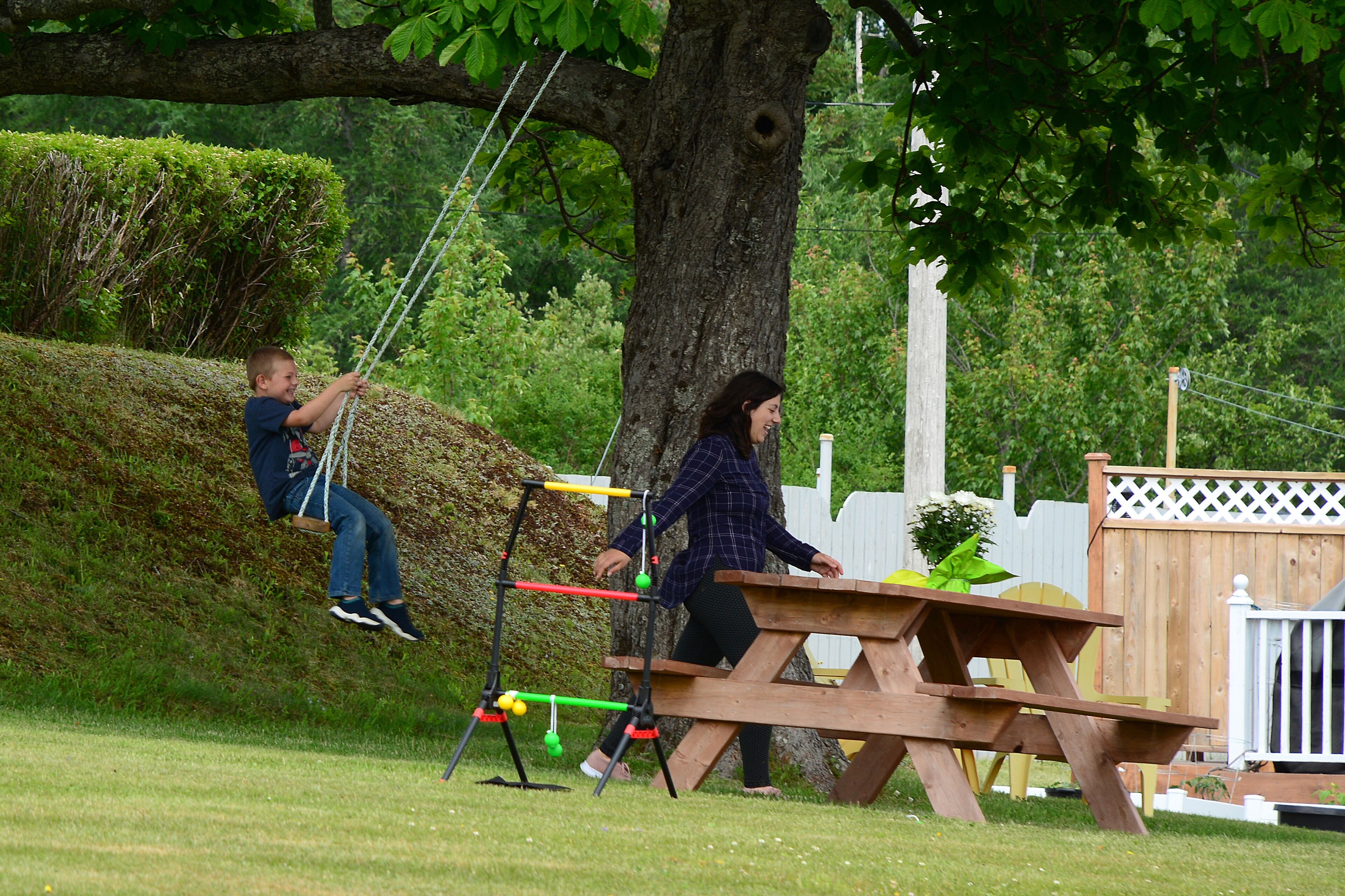Een picknicktafel en schommelset in een grasveld, met een boom en een houten hek op de achtergrond.