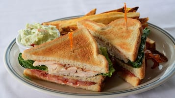 A sandwich cut in half with bacon, lettuce, and tomato, served with a side of coleslaw and fries on a plate.