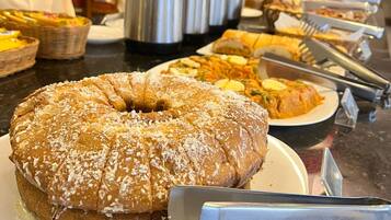 Buffet com diversos pratos, incluindo um bolo grande com coco ralado e um espaço para café com vários potes térmicos.