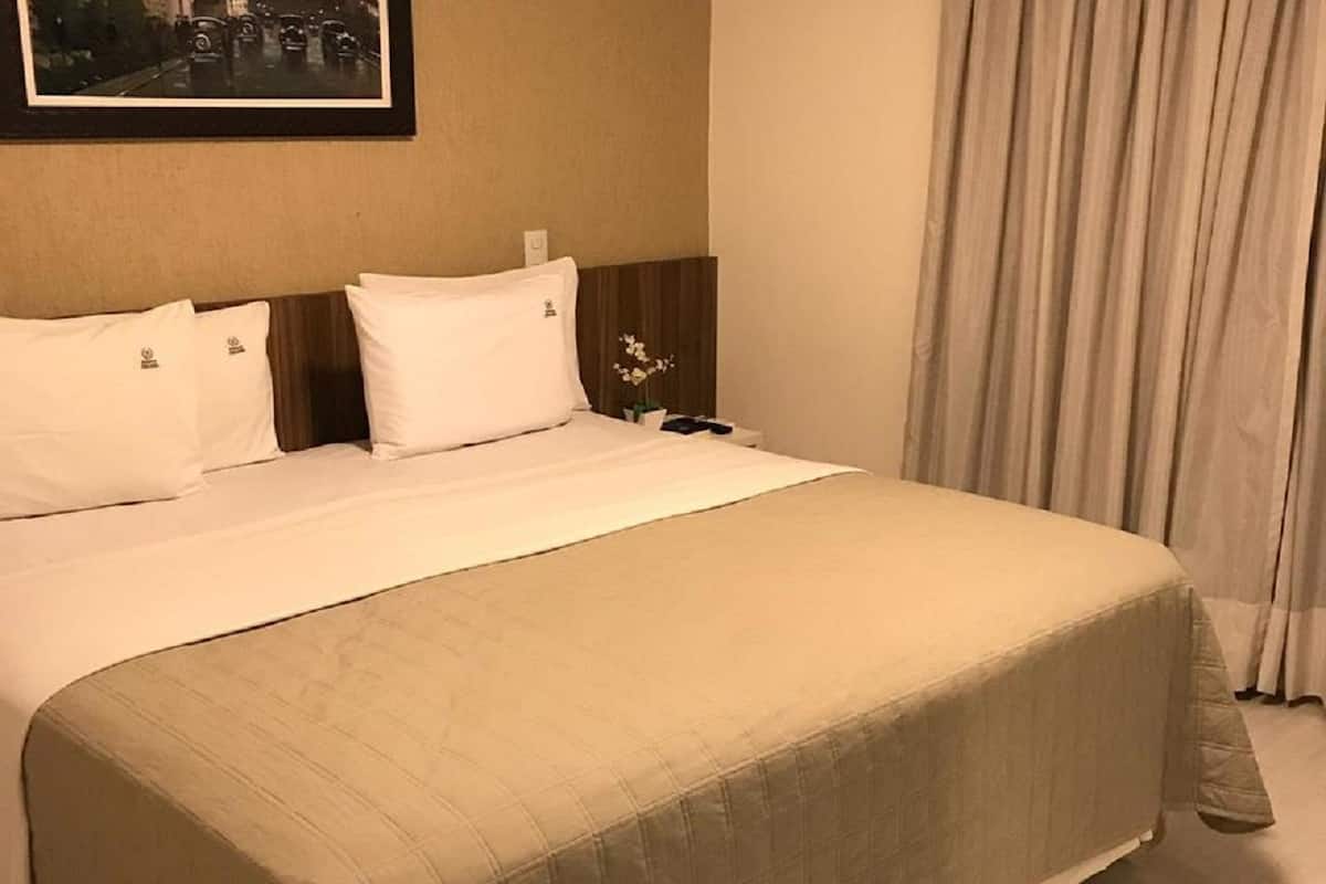 A hotel room with a large bed, a nightstand, a framed picture on the wall, and a window with curtains.