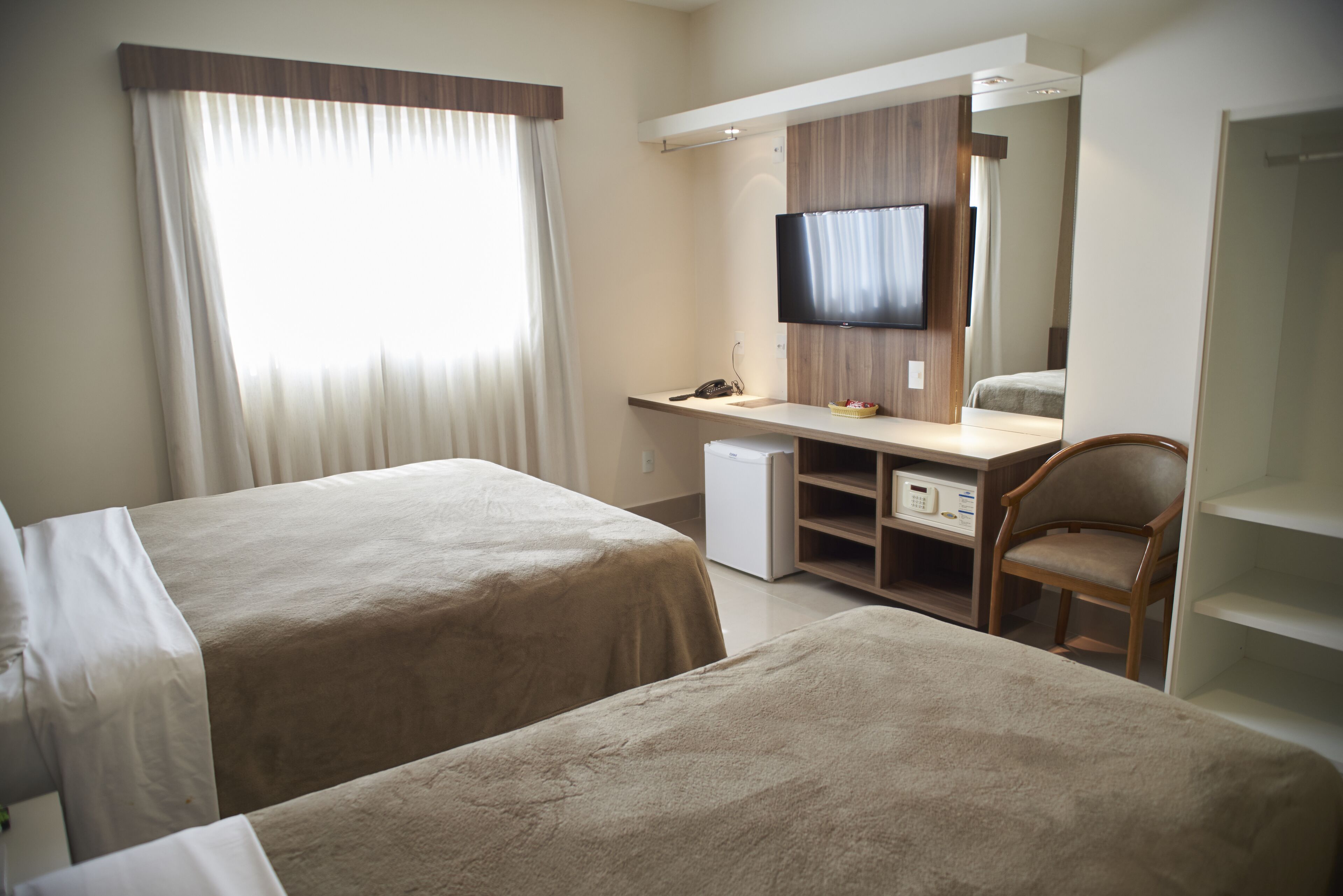 Ett hotellrum med två sängar, ett skrivbord med en dator, en stol, en tv och ett litet kylskåp.