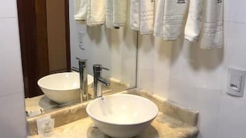 A bathroom with a large white sink, a mirror, and multiple white towels hanging on the wall.