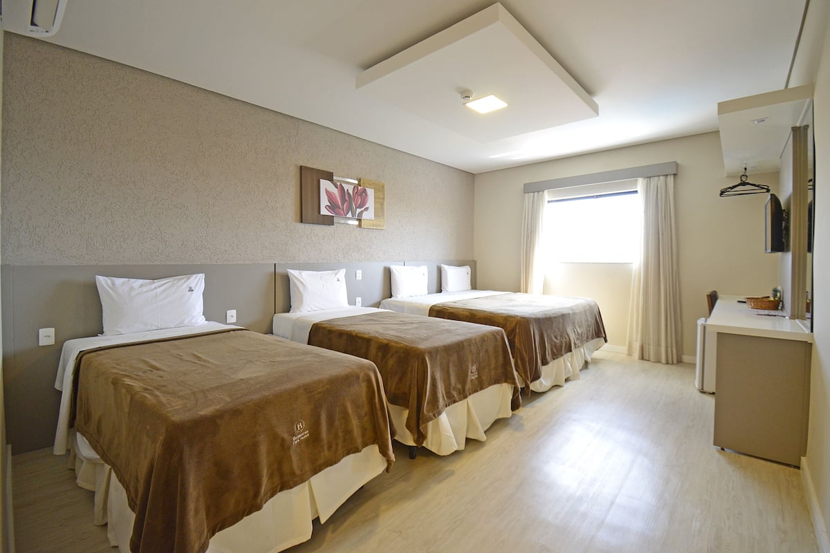 A hotel room with two beds, a desk, and a window with curtains.