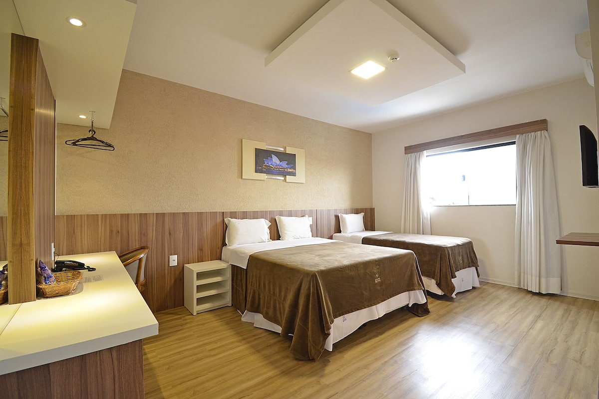 A hotel room with two beds, a wooden floor, a wall-mounted picture, and a window with curtains.