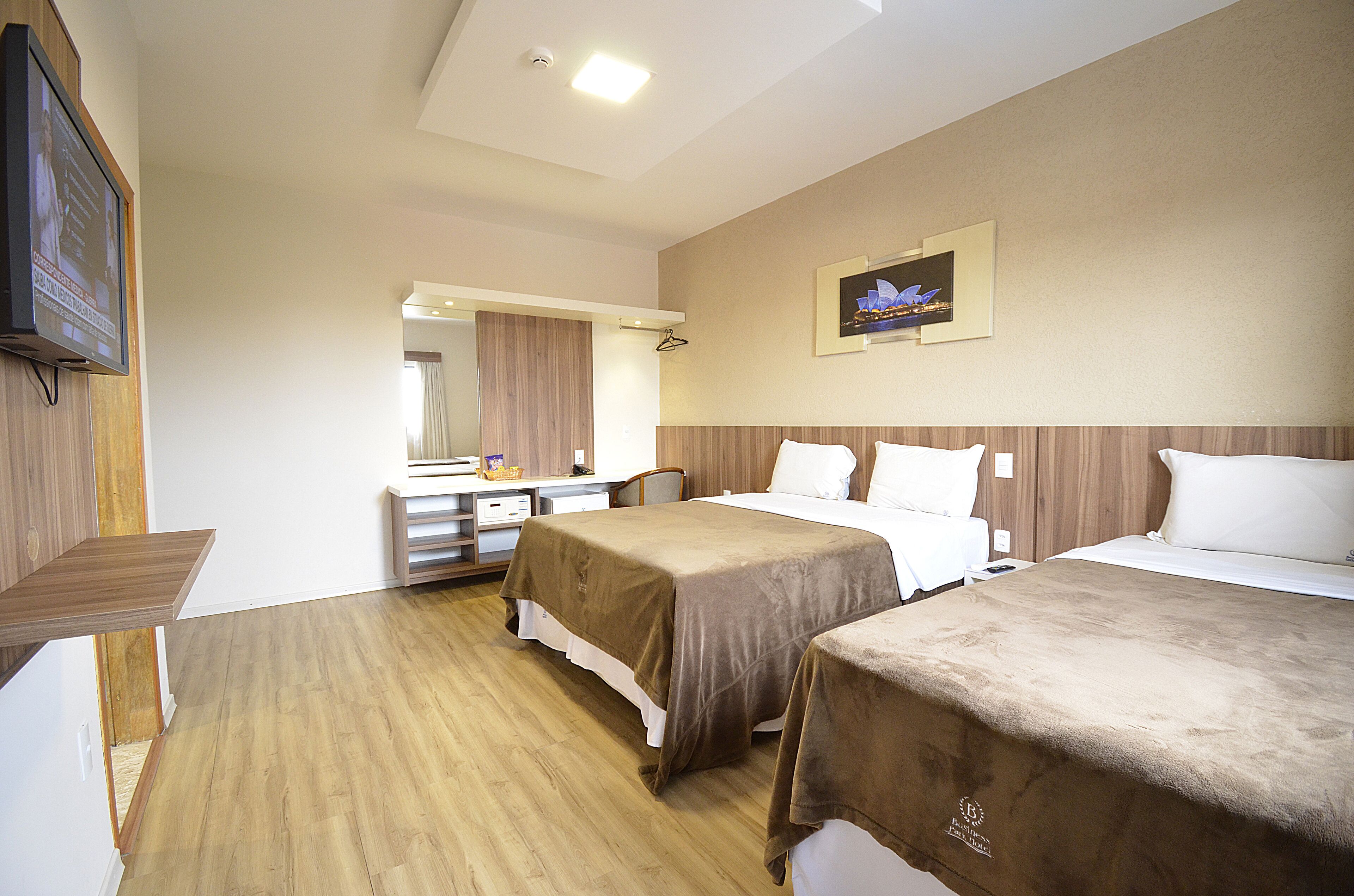 Habitación de hotel con dos camas, un escritorio, una silla, un televisor y un cuadro en la pared.