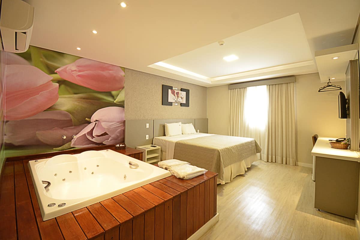 A hotel room with a large bathtub, a bed, a desk, and a mirror.
