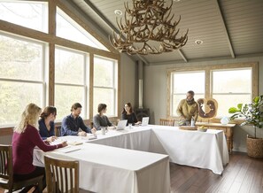 A conference room with large windows, a chandelier, and a table with people working.