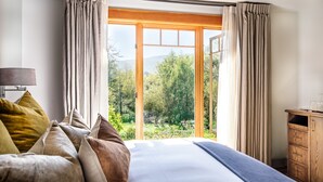 A bedroom with a large bed, a wooden dresser, and a view of a garden through a sliding glass door. - Olema House at Point Reyes (Olema)