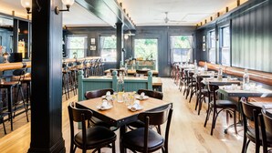 A restaurant with wooden tables and chairs, a bar area, and large windows. - Olema House at Point Reyes (Olema)