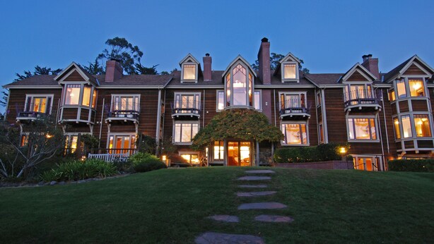 A large, multi-story wooden house with multiple balconies and large windows, surrounded by a well-maintained lawn and a stone pathway leading to the entrance. - Olema House at Point Reyes (Olema)