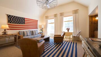 Un salon comprenant un grand drapeau américain, un canapé, une table basse, un fauteuil et un tapis à rayures.