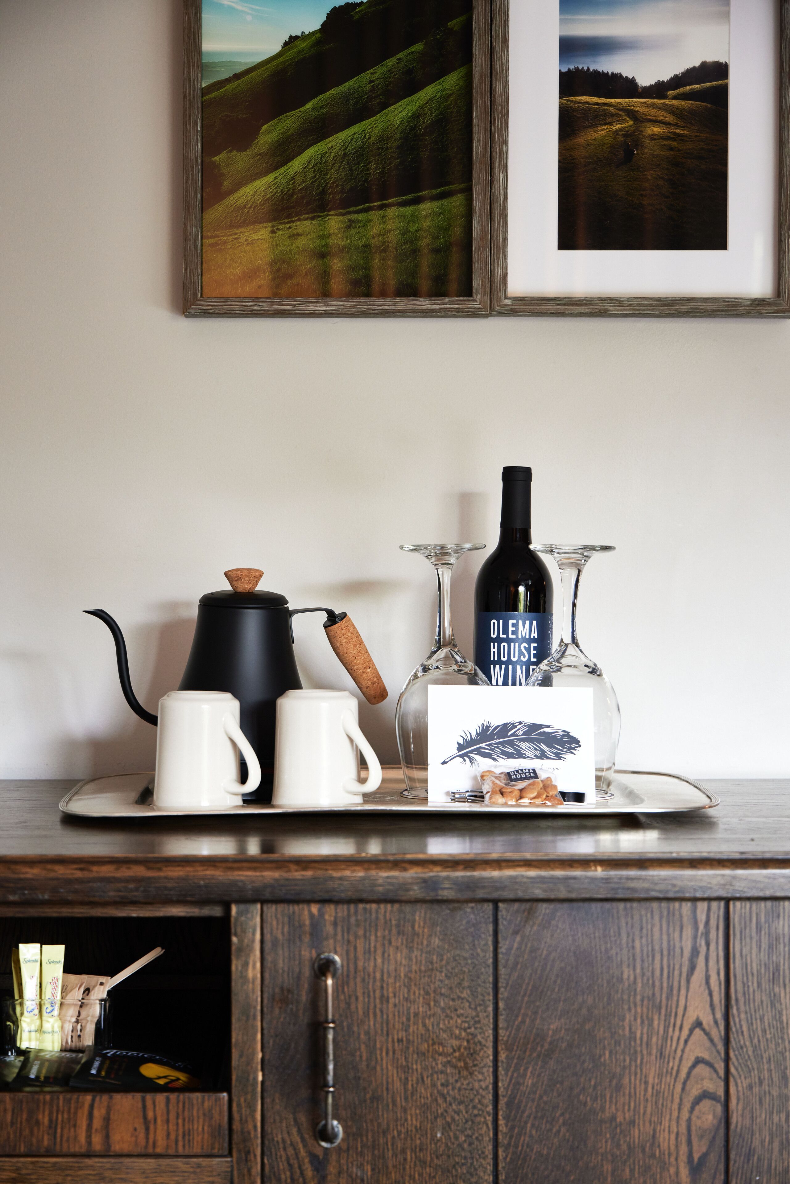 Un piano di lavoro in cucina con una macchina da caffè, due tazze bianche, una bottiglia di vino e due bicchieri da vino.