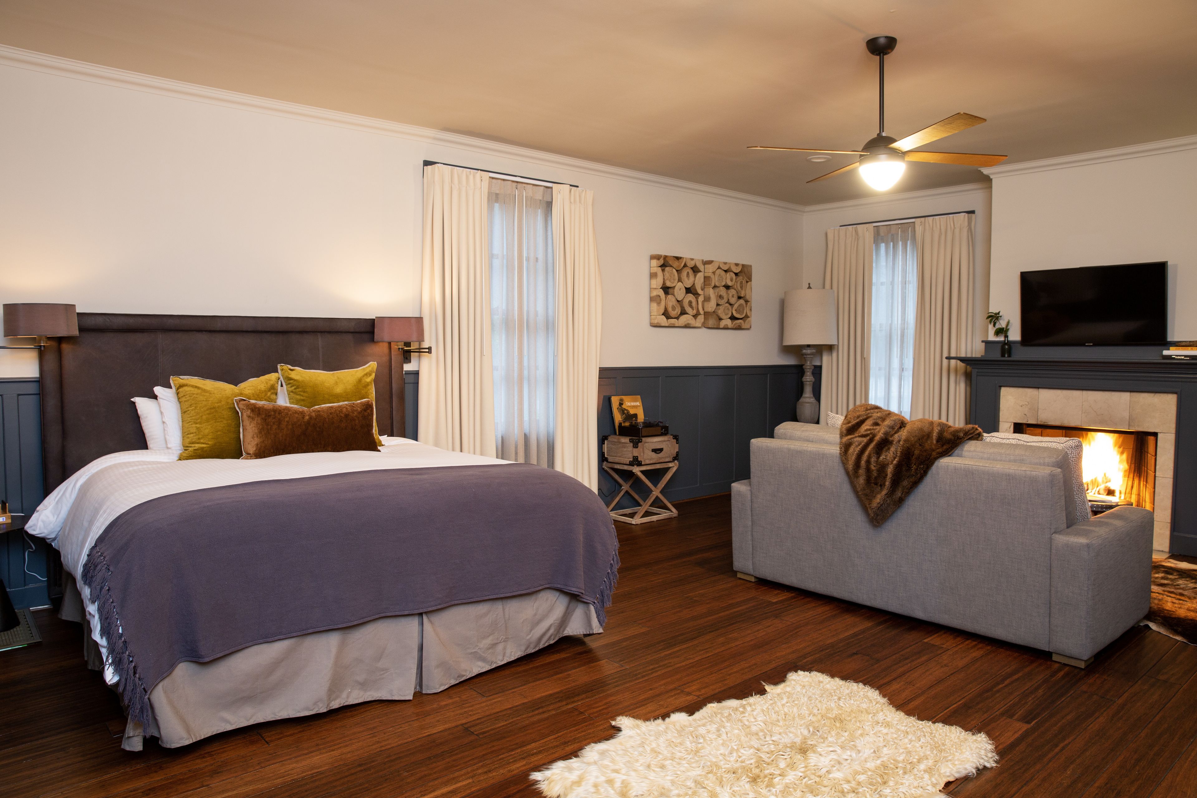 A bedroom with a bed, a grey sofa, a fireplace, and a television.