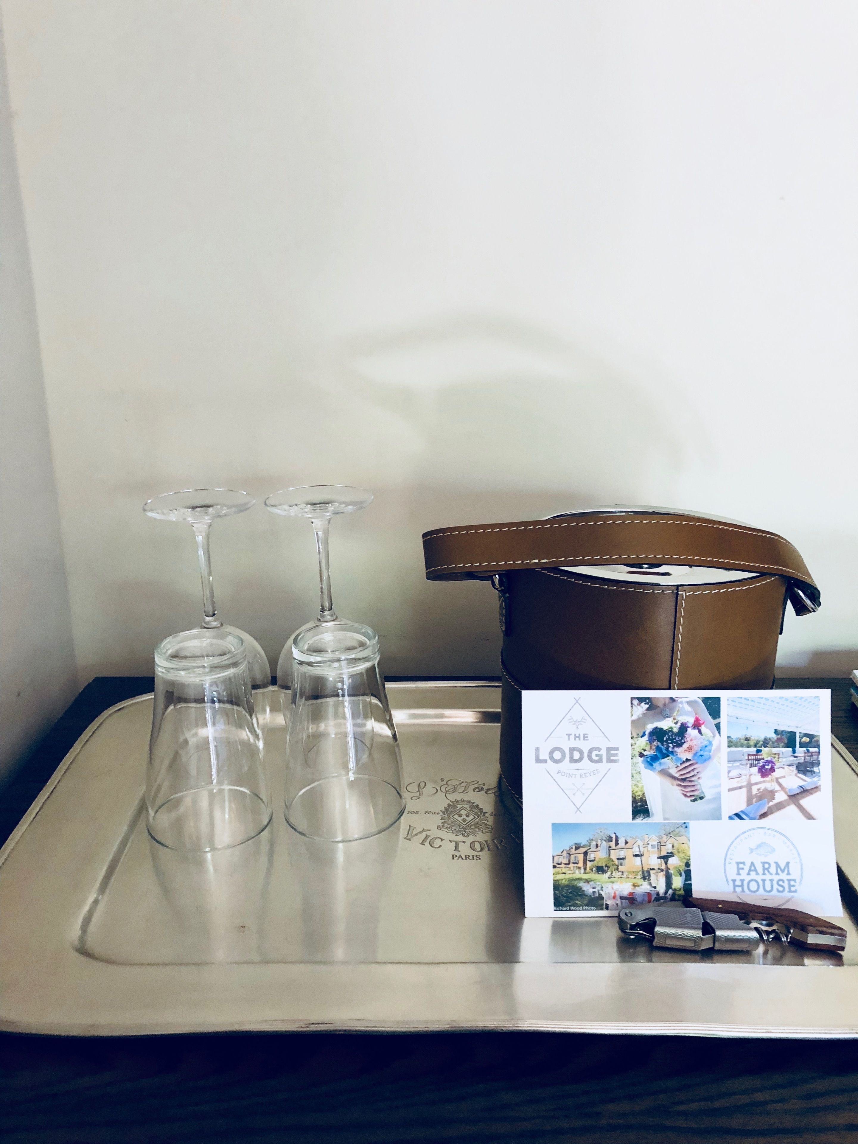 A tray with three wine glasses and a brown leather bag with a booklet titled "The Lodge" on a table.