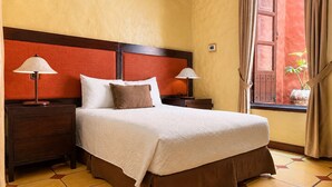 A hotel room with a large bed, two bedside tables with lamps, a window with curtains, and a view of the outside. - 1915 Hotel (Alajuela)