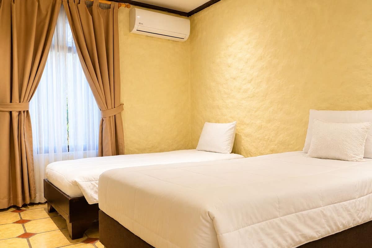 A hotel room with two beds, beige walls, and an air conditioning unit.