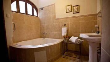 A bathroom with a large bathtub, a pedestal sink, and two framed pictures on the wall.