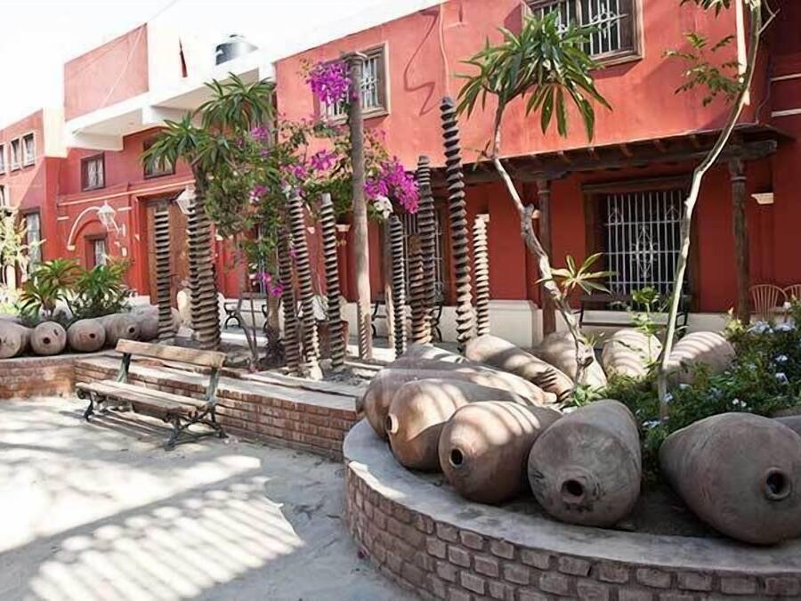A courtyard with a red building, large stone sculptures, and some greenery.