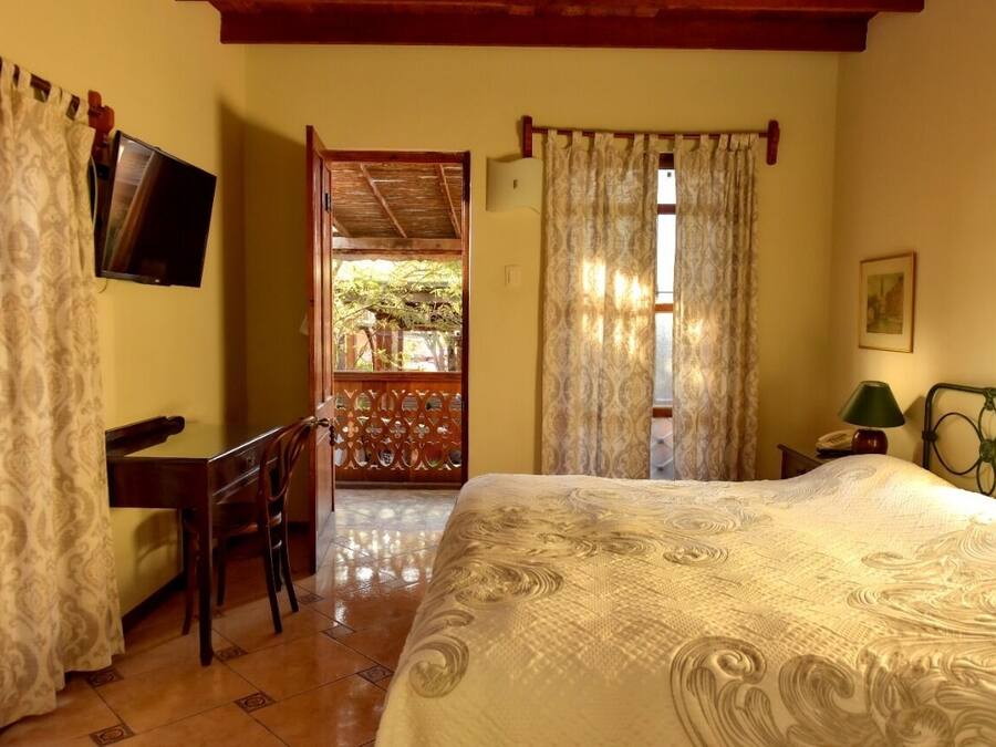 Un dormitorio con cama, escritorio, silla, televisor y ventana con cortinas.