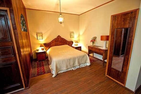 A bedroom with a wooden bed, bedside lamps, a nightstand, and a mirror.