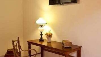 Una habitación pequeña con un escritorio de madera, una silla, una lámpara y un televisor de pantalla plana montado en la pared.