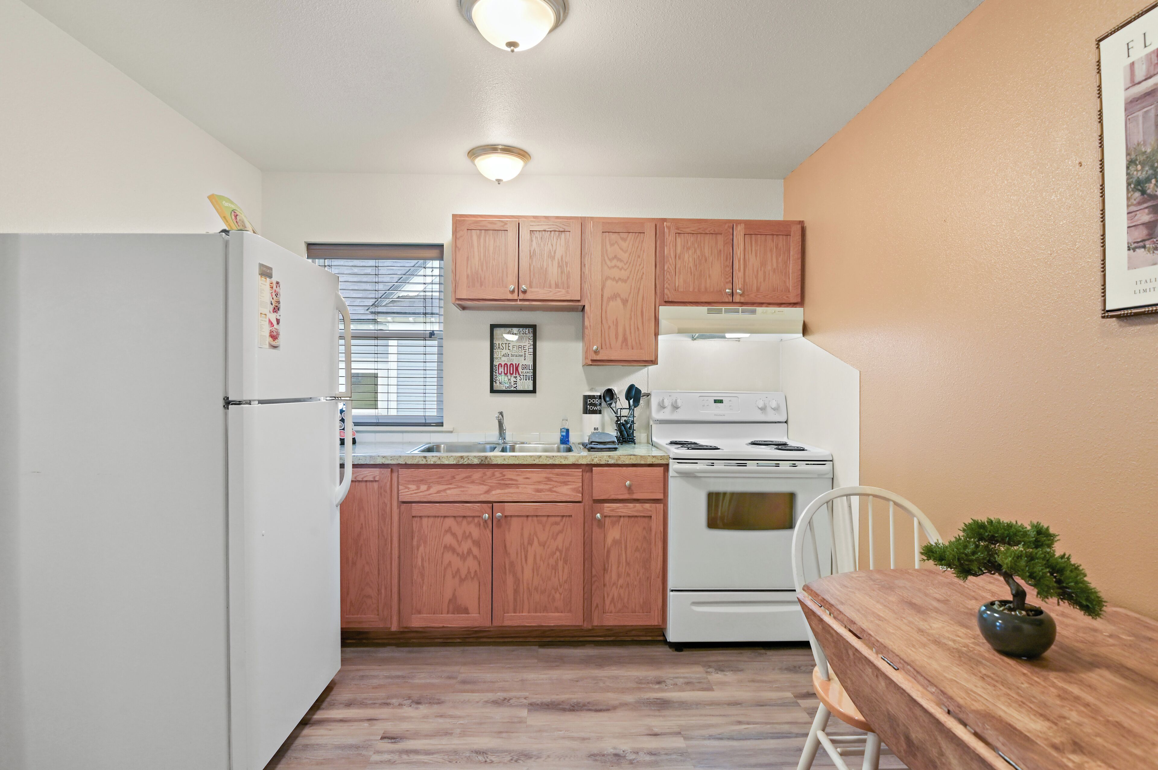 A kitchen with wooden cabinets, a white refrigerator, a stove, and a dining table with a potted plant.