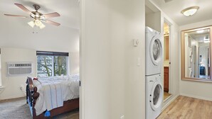 A bedroom with a bed, a ceiling fan, a washing machine, and a large mirror. - Maple Leaf Manor Suites (Spokane)