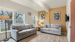 A living room with two grey sofas, a floor lamp, and abstract wall art. - Maple Leaf Manor Suites (Spokane)