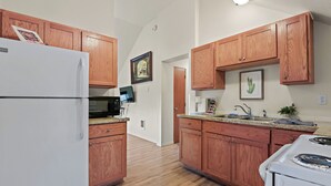 A kitchen with wooden cabinets, a refrigerator, a microwave, a stove, and a sink. - Maple Leaf Manor Suites (Spokane)