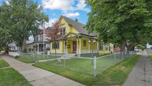 A yellow house with a porch, surrounded by a chain-link fence, and a sidewalk in front. - Maple Leaf Manor Suites (Spokane)