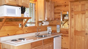 A compact kitchen with wooden cabinets, a microwave, a sink, a coffee maker, and a refrigerator. - Smoky Bear Ranch Bed & Breakfast & Cabins (Columbia Falls)