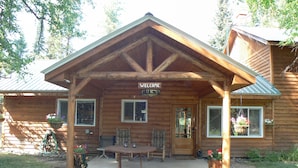 A wooden cabin with a 'Welcome' sign, a covered porch, and a table with chairs. - Smoky Bear Ranch Bed & Breakfast & Cabins (Columbia Falls)