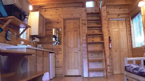 A wooden cabin interior with a kitchen area, a dining table, and a bed. - Smoky Bear Ranch Bed & Breakfast & Cabins (Columbia Falls)