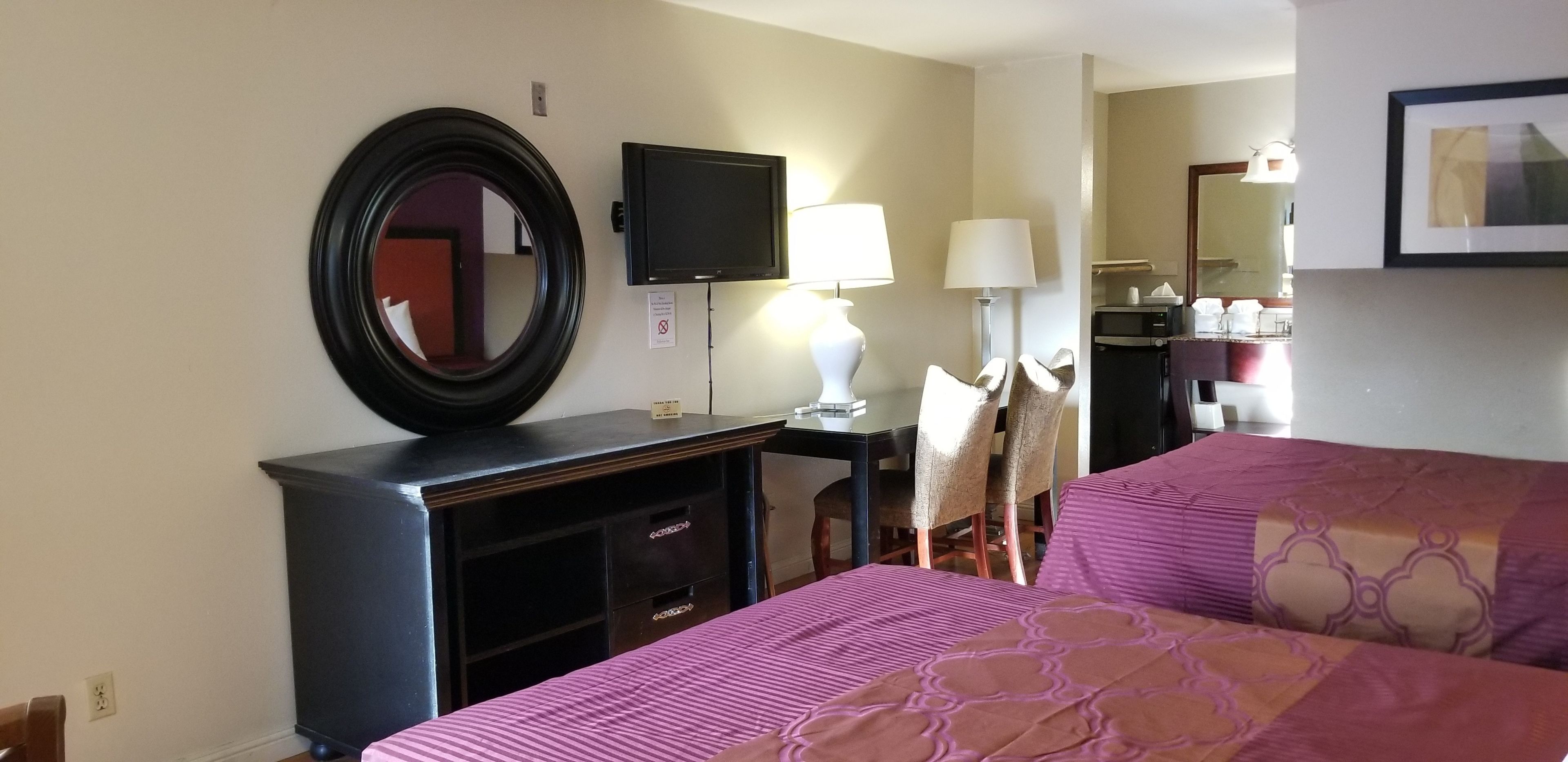 Une chambre d’hôtel avec deux lits, un bureau avec un ordinateur, une télévision et un miroir.
