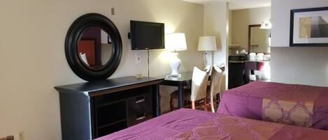 Une chambre d’hôtel avec deux lits, un bureau avec un ordinateur, une télévision et un miroir.