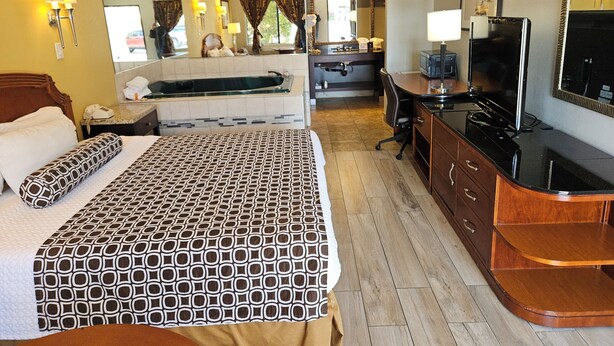 A hotel room with a bed, a desk, a TV, and a bathroom with a bathtub. - Fullerton Inn - Near Medieval Times (Fullerton)