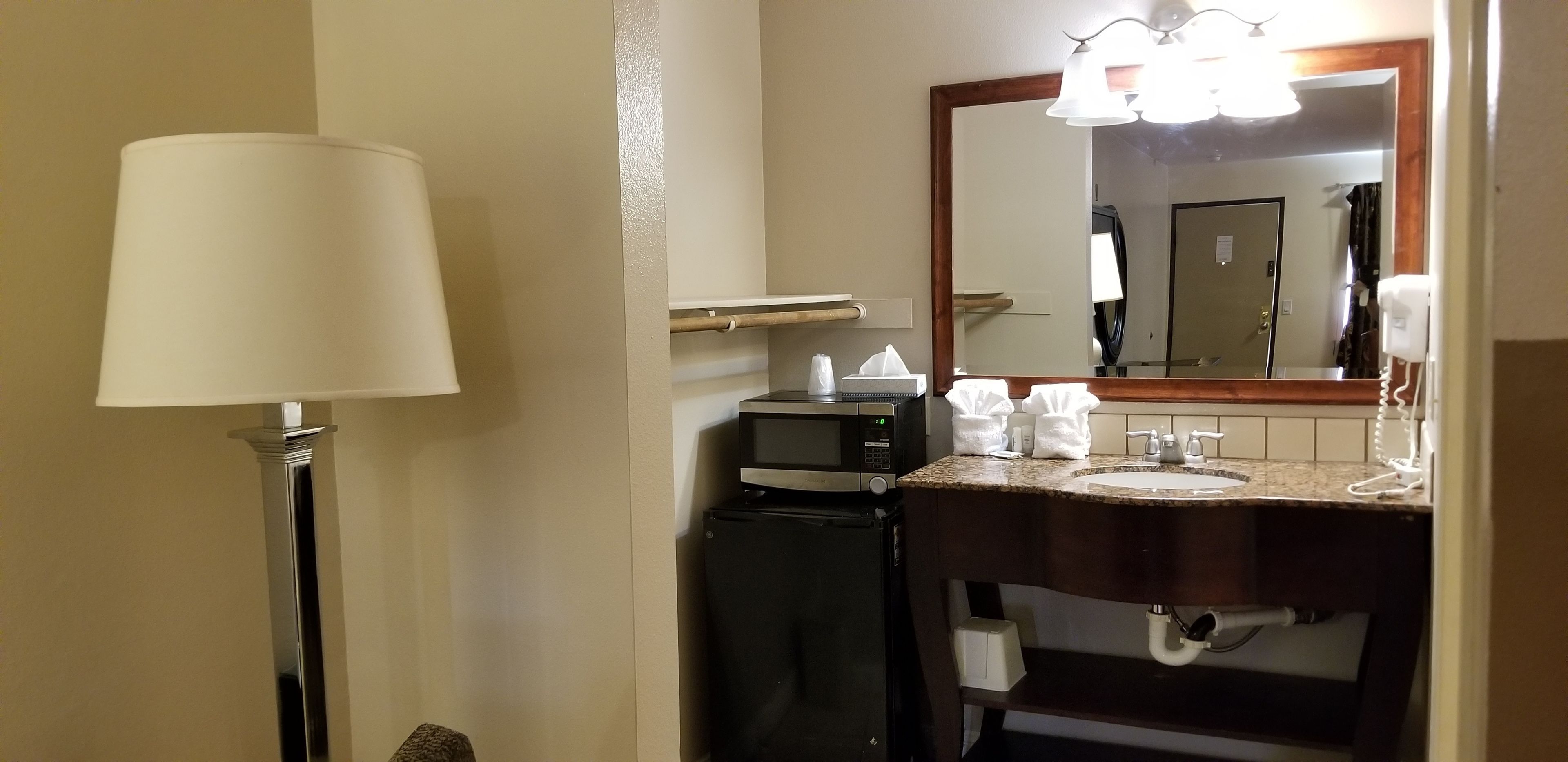 Een hotelbadkamer met een wastafel, spiegel, zeepdispenser en een magnetron.