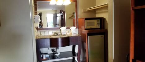 A compact bathroom with a sink, mirror, and a small refrigerator.