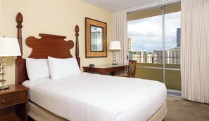 Ein Hotelzimmer mit einem großen Bett, einem Schreibtisch, einem Stuhl, einer Lampe und Blick auf die Stadt durch ein großes Fenster.
