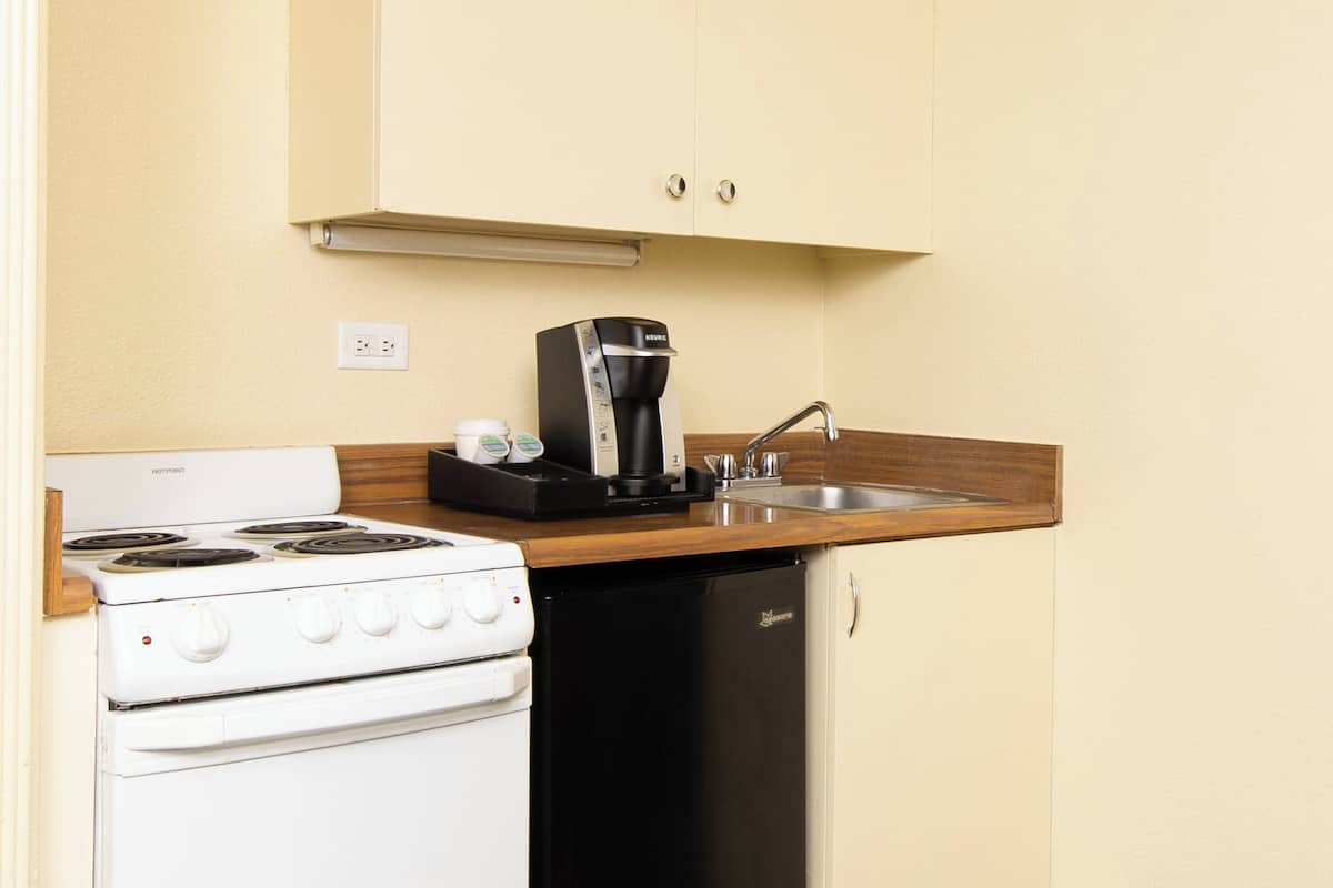 A compact kitchenette with a white stove, black dishwasher, and a coffee maker on the countertop.