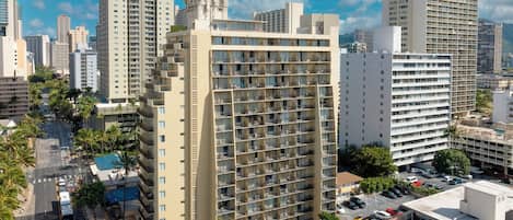 A high-rise hotel with multiple balconies, a rooftop pool, and a view of the surrounding cityscape.