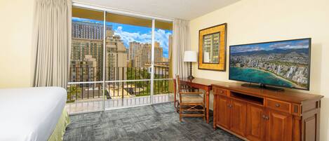 A hotel room with a bed, a desk, a television, and a large window with a city view.