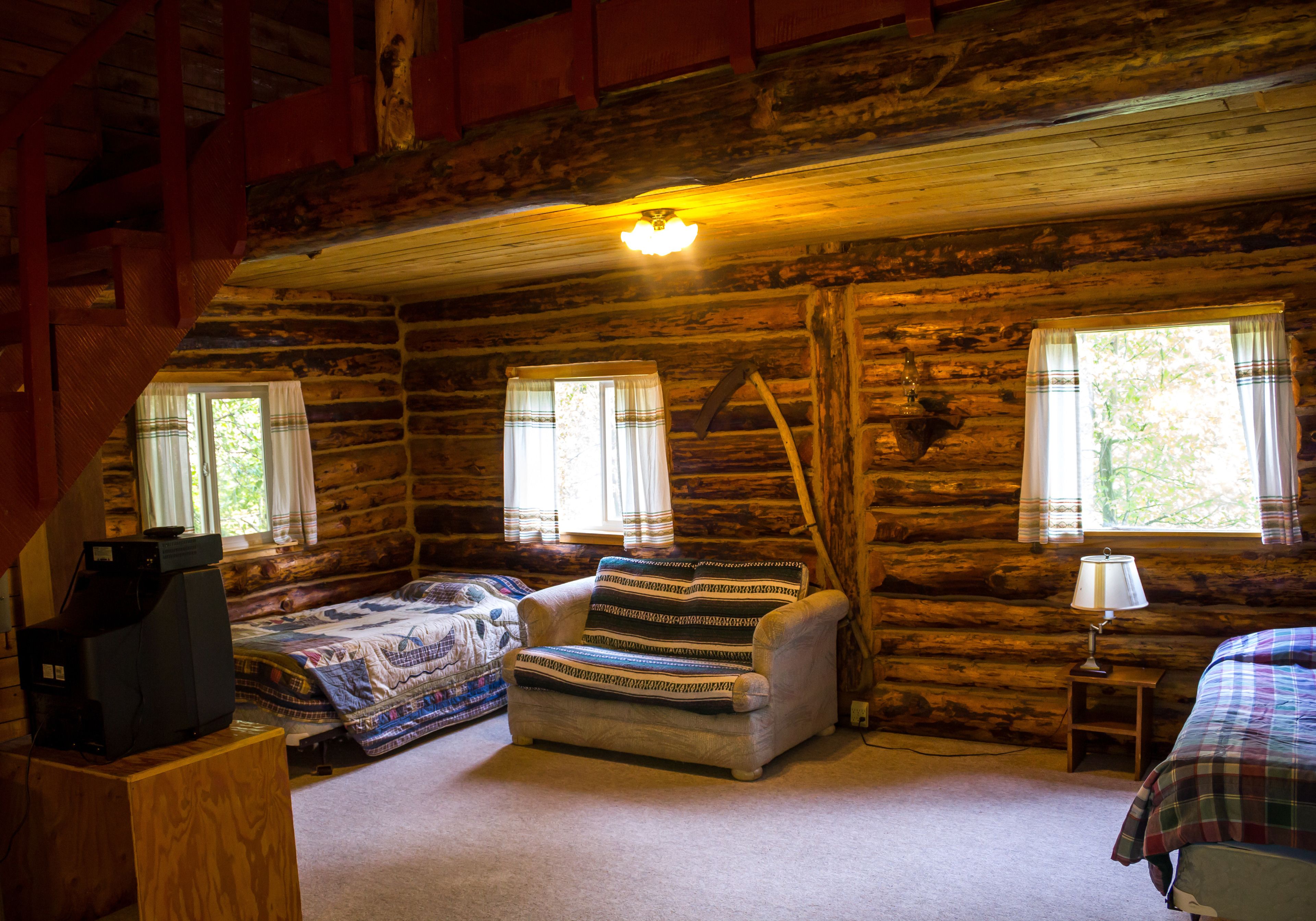 A log cabin room with a bed, a chair, a television, and a lamp.