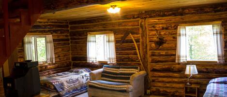 A log cabin room with a bed, a chair, a television, and a lamp.